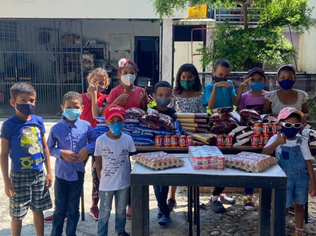 A group of children stand behind tables with food supplies during a community aid activity in Venezuela.