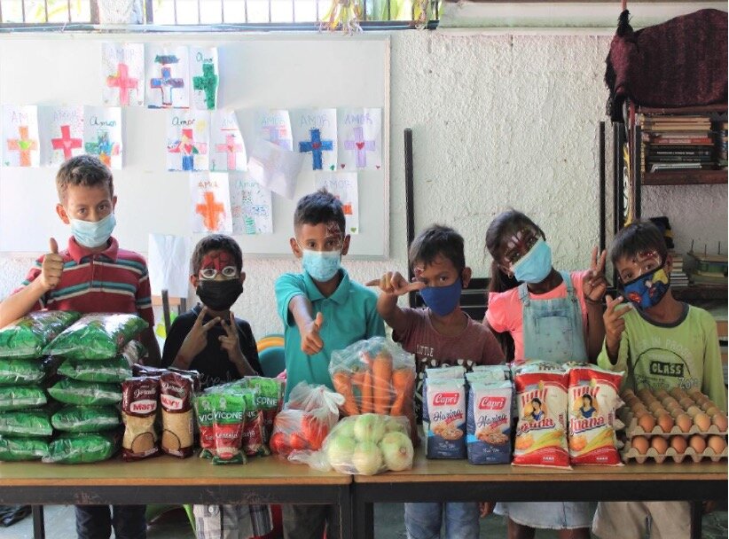 A group of children stand behind a table filled with food and basic supplies during a community aid activity in Venezuela.
