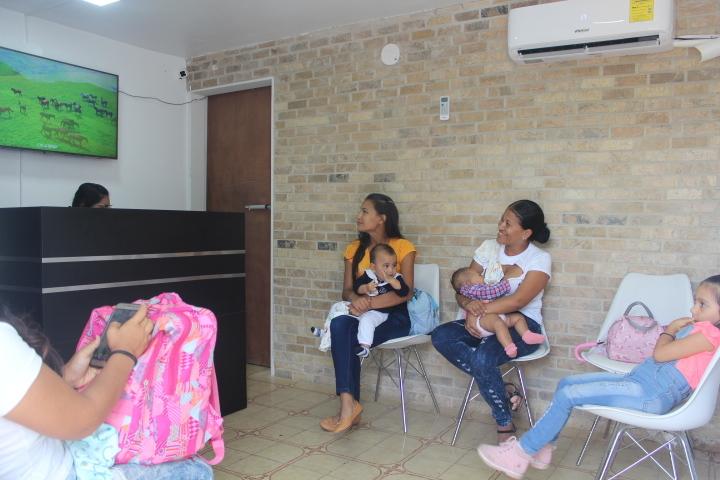 Mothers and children sit in the waiting area at SAI Medical Clinic, where a TV is provided for patients in the waiting room.