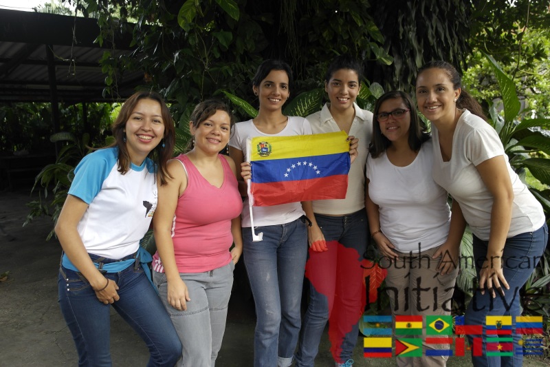 A group of smiling women holding the Venezuelan flag during an SAI community support mission.
