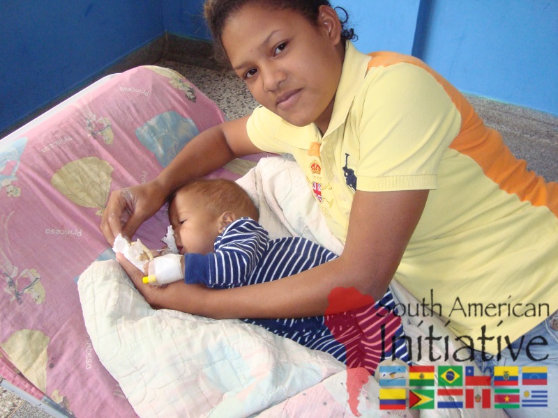 A caregiver holding a resting child in a hospital area while receiving support connected to SAI in Venezuela.
