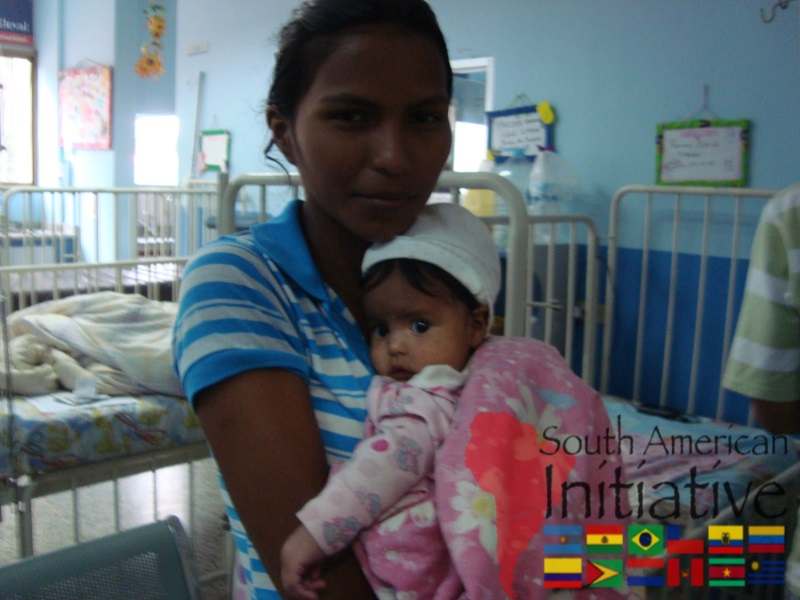A young woman holding an infant inside a pediatric care area in Venezuela supported by SAI.