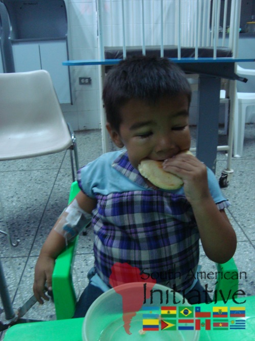 A young child eating food while seated in a hospital area supported by SAI in Venezuela.