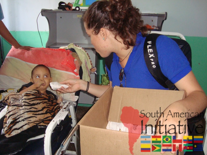 An SAI volunteer bringing support items to a child resting in a hospital bed in Venezuela.