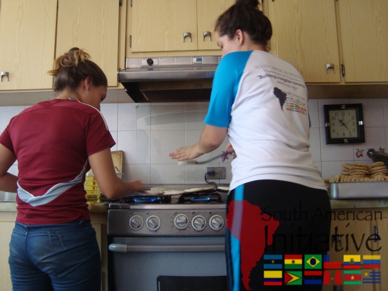 Two SAI volunteers cooking arepas in a kitchen to help feed families in Venezuela.