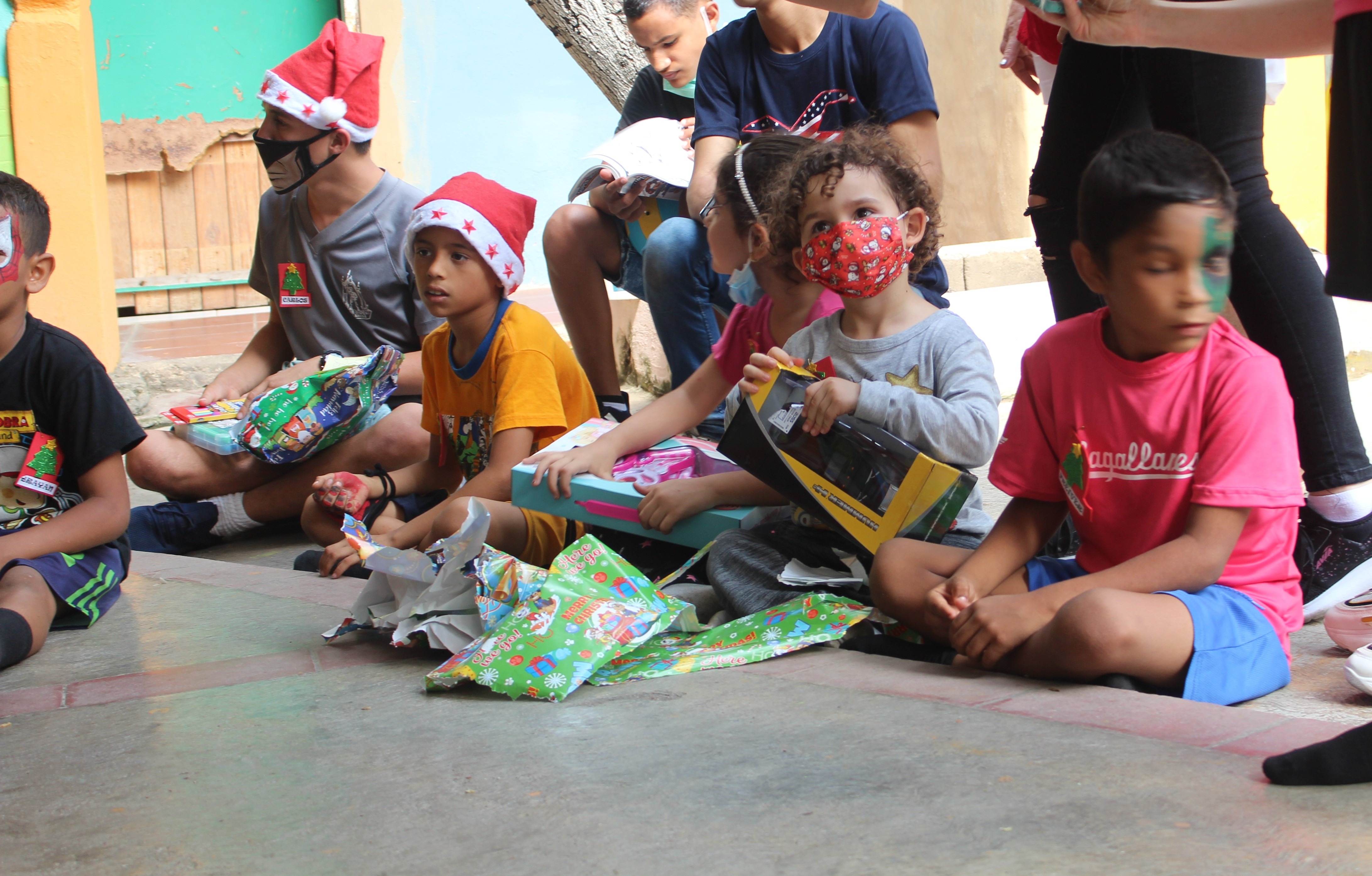 Children sitting together outdoors while opening gifts during an SAI community celebration in Venezuela.
