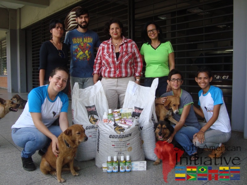 A group of volunteers and staff pose with rescued dogs, pet food, and medical supplies in Venezuela.