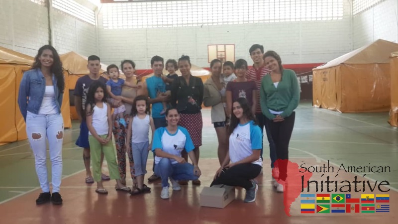 Refugees and volunteers stand together inside an emergency shelter with  tents in Venezuela.
