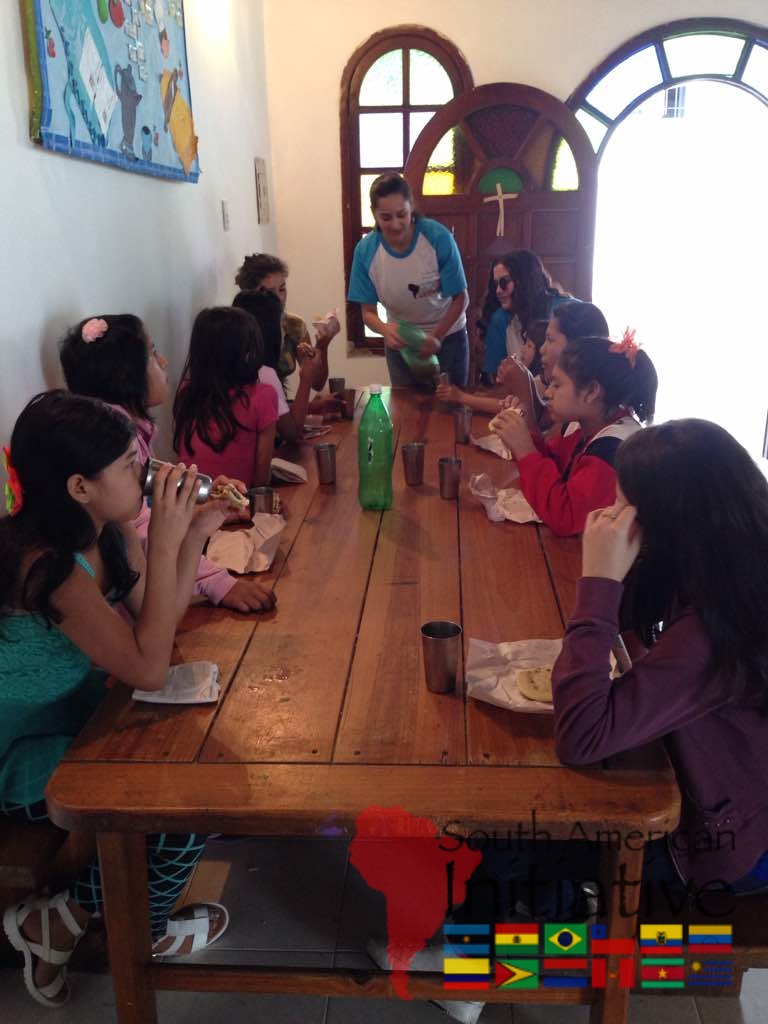 SAI volunteers serve and share a meal with children gathered around a table in Venezuela.
